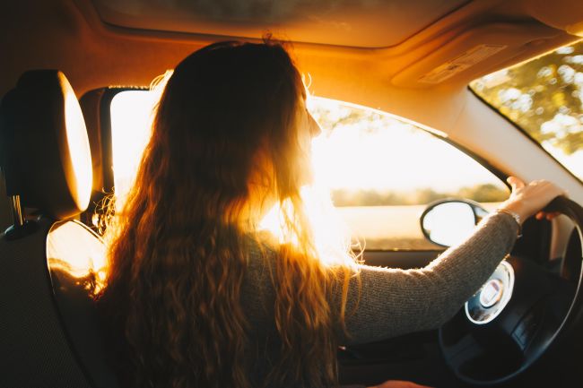 Woman with long hair driving a vehicle, sunshine coming through the window behind her profiled face.