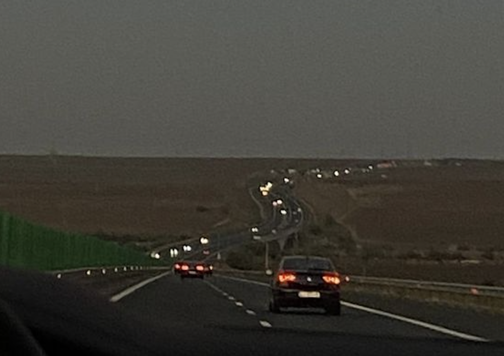 A view from a car driving at night on a highway with cars ahead getting smaller and smaller in the distance.